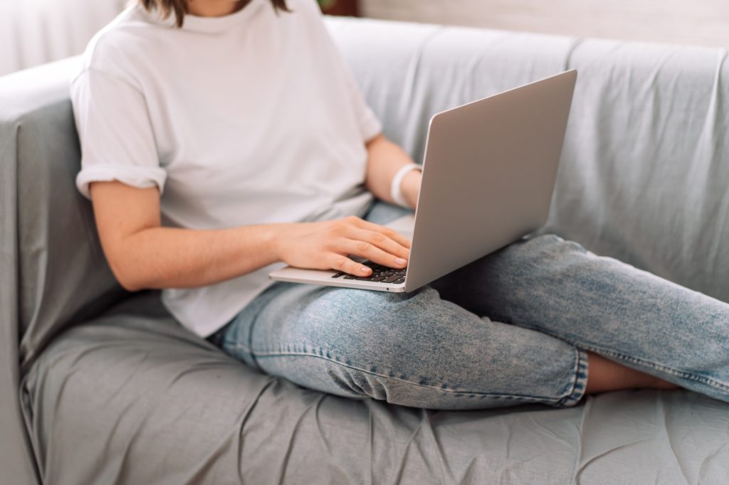 Lady psychologist sitting on gray sofa working with laptop
