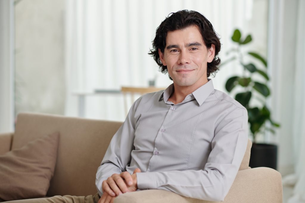 Young smiling businessman, blogger or psychologist sitting on couch
